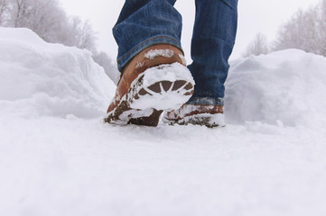 Man walks with boots through deep snow in  winter day.