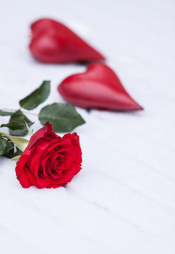 Eine rote Rose und zwei rote Herzen im Schnee, vertikal