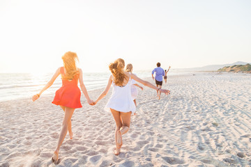A group of friends runs on the deserted beach at sunset in the direction of the sunset. The last...
