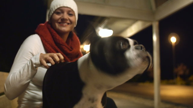 Dog with Female Owner at Night. Pretty Young Woman with Boston Terrier on City Bench