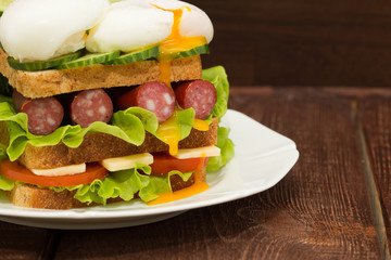 Sandwich with tomatoes, cucumbers, sausages, salad and poached eggs