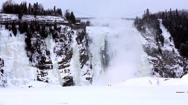 Young adventurers play in the snow and ice and are dwarfed by the frozen Monmorency Falls, Quebec City, Canada