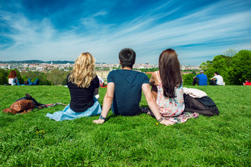 Three tourists friend sitting on the green grass with beautiful view to Vienna panorama