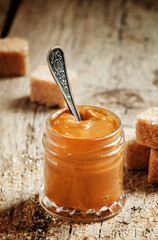 Sweet liquid caramel in a small jar and brown cane sugar, on the