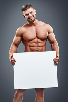 Muscular young man holding blank white poster