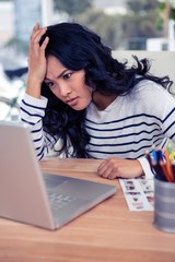 Concentrated Asian woman with hand on head looking at laptop