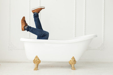 Feet in jeans and gym shoes looking out of a white bath in a whi
