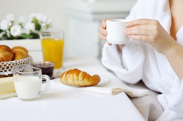 Beautiful woman drinking hot drink at the table with a croissant.