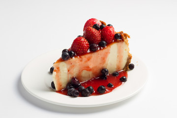 Slice cheesecake with blueberries and strawberry on white plate closeup