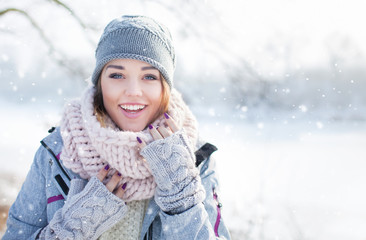 Fototapeta na wymiar Beautiful happy laughing young woman wearing winter hat gloves and scarf covered with snow flakes. Winter forest landscape background