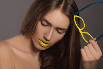 Beauty woman face portrait with yellow lips. Model holding a yellow glasses