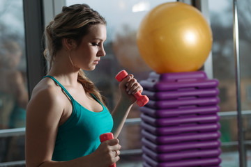 Beautiful sportswoman doing exercise with dumbbell for biceps in fitness center