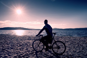 Fototapeta premium Young man cyclist silhouette on blue sky and sunset background on the beach. End of season at lake.