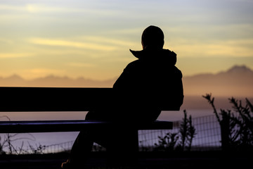 Fototapeta na wymiar Silhouette of man on bench watching sunset