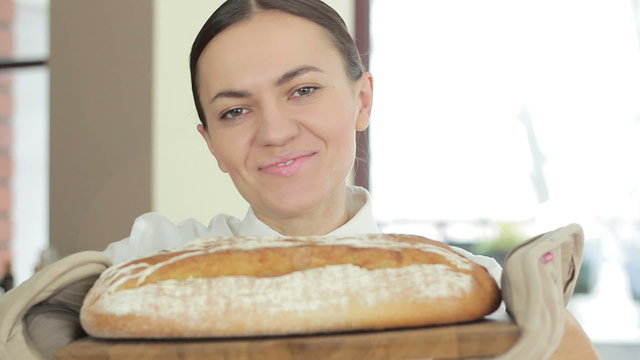 A young smiling woman standing in her kitchen holding freshly baked bread, close up