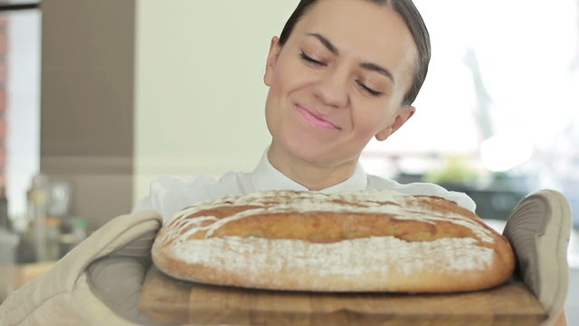 A young smiling woman standing in her kitchen holding freshly baked bread, close up