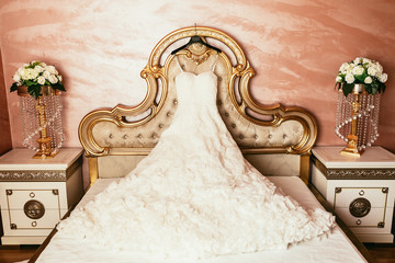 wedding dress hanging on luxury bed decorated with flowers