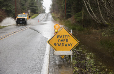 Emergency vehicle driving on flooded road with warning sign