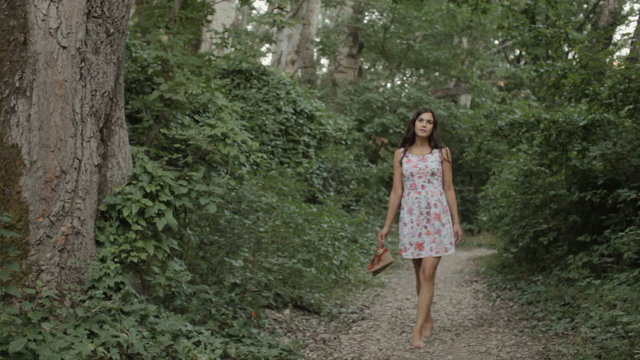 Brunette in a dress goes barefoot on the road in the forest