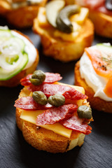 Small canape with grilled baguette with the addition of sausage, capers on  stone black background