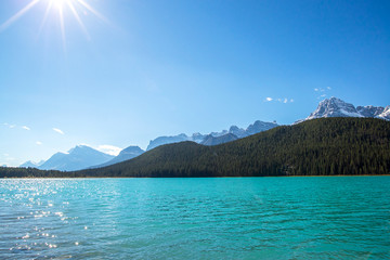 turquoise waters of a lake in front of a forest and a peak in the rocky mountains of alberta canada