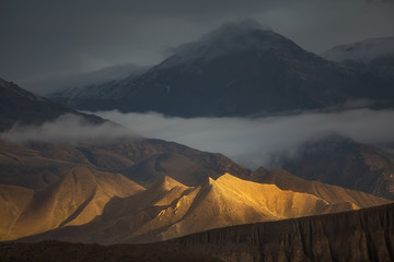Golden Hills. Beautiful natural scenery. Hills brightly lit by the sunlight with dramatic mountain view on the backside. Captured in Upper Mustang region, Himalayas, Nepal. - 100850681
