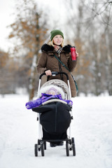 Fototapeta na wymiar Young mother walking with baby in stroller in winter