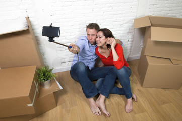 Fototapeta na wymiar young happy American couple sitting on floor celebrating moving to new house taking selfie photo with mobile phone