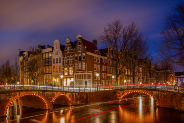 Night view over Amsterdam canals and bridges, with lights and their trails