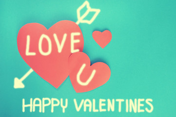 Writing Love you and arrow on red hearts paper on cyan paper bac