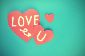Writing Love you on red hearts paper on cyan paper background fo
