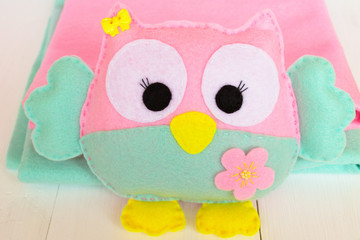 Felt owl on a white wooden background, rolls of pink and blue felt 