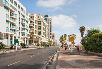 Highway along embankment with buildings on road side, parking and people walking along. Tel Aviv, Israel.
