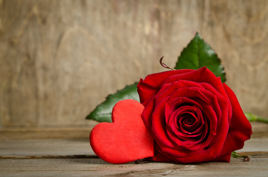 Beautiful rose and one handmade heart  on the wooden board surfa