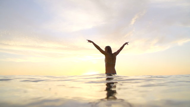 Young Happy Woman Celebrating at Sunset With Hands Up In Air on Surfboard. 
