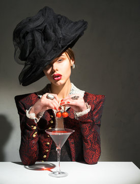 Woman in a hat drinking a martini with a cherry