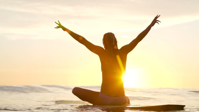 Young Happy Woman Celebrating at Sunset With Hands Up In Air on Surfboard. 
