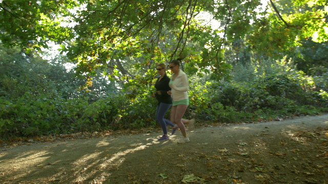 Two Women Jogging in Park on Sunny Day. Brunette and Blond Young Joggers on Forest Trail with Sun Flares