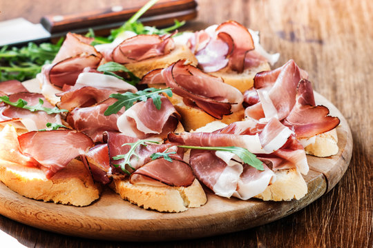 Slices of Prosciutto on old wooden background.