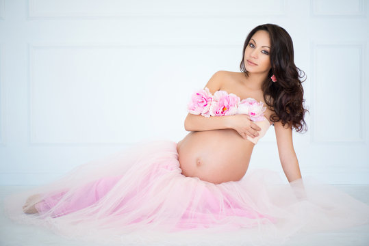 Gentle photo of pregnant girl in tulle skirt and pink peonies