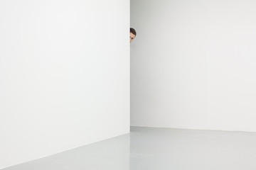 Man in white room looking from behind corner
