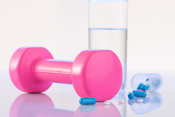 Dumbbell, pills and glass of water on the surface. 