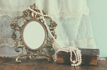 Antique blank Victorian style frame and old book with vintage pearl necklace on wooden table. retro...