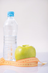 Bottle of water with apple and measuring tape. 