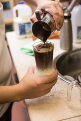 Barista pouring milk in capuccino coffee in coffeeshop