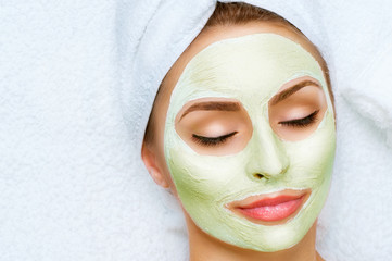 Portrait of beautiful girl with a towel on her head applying facial mask