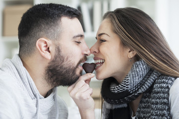 Portrait of young adult caucasian eating a heart chocolate cookie. Valentines couple sharing cookie

