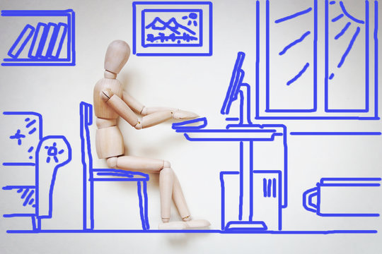 Man working with his computer by the table. Abstract image with a wooden puppet