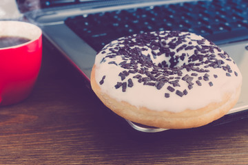 donut, coffee and a laptop on an old wooden table, toned