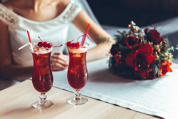 Beautiful red cocktail with cherries and wedding rings, behind the bride with a wedding bouquet of red roses